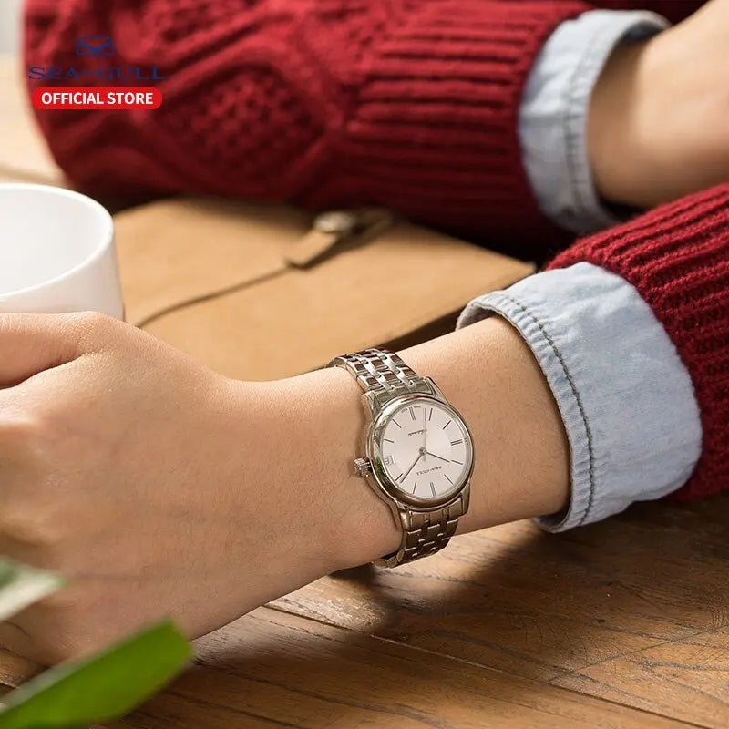 Eleganty Armbanduhr mit weißem Zifferblatt und Edelstahlarmband am Handgelenk, kombiniert mit rotem Pullover.