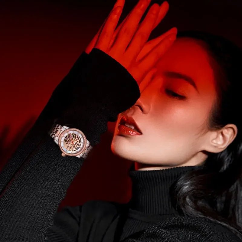 alt
Donna elegante che indossa un orologio con quadrante scheletrato e dettagli in oro rosa sotto illuminazione rossa